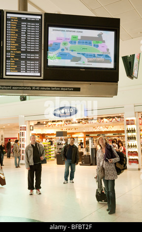 I viaggiatori guardando le partenze bordo terminale in una lounge di partenza, l'aeroporto di Heathrow di Londra, Regno Unito Foto Stock