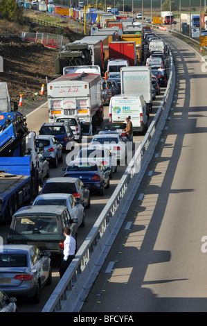Automobilisti fuori dai veicoli che si appoggiano sulla barriera di collisione traffico bloccato a griglia autostrada M25 in lavori stradali chiusi a causa di incidenti volti oscurati e numeri UK Foto Stock