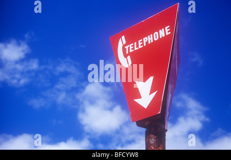 Segno rosso con icona del telefono e il telefono di parola con la freccia rivolta verso il basso appollaiato sul palo arrugginito sotto il cielo blu con nuvole bianche Foto Stock