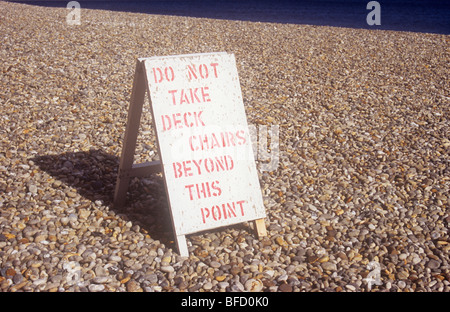 Sandwich-board seduto su una vasta distesa di spiaggia ghiaiosa dichiarando Non prendere Sdraio oltre questo punto Foto Stock