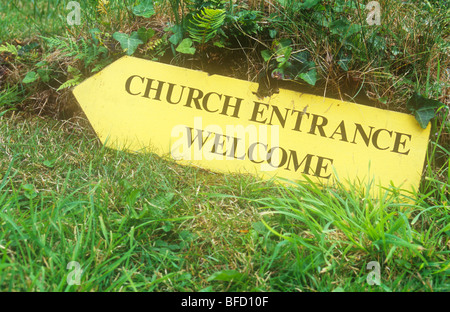 Giallo scheda fingerpost giacente sulla banca di erba rivolta verso sinistra e affermando Chiesa Benvenuto di ingresso Foto Stock