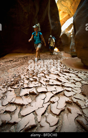 Un uomo e una donna escursioni attraverso uno stretto canyon passato essiccato incrinato e fango in Utah. Foto Stock