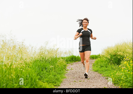 Giovane donna in esecuzione sul sentiero di ghiaia attraverso un luminoso verde campo in spirito Mound, South Dakota. Foto Stock