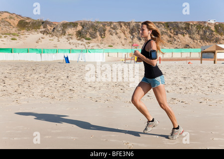 Giovane donna nel suo 20's fa avanzare su una spiaggia un lettore musicale attaccata al suo braccio - modello di rilascio disponibili Foto Stock