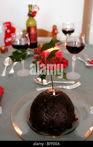 Un pudding natalizio con holly su un tavolo da pranzo prevista per la cena di Natale. Foto Stock