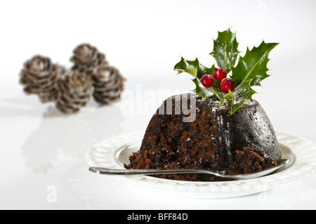 Pudding natalizio con holly, coni in background Foto Stock