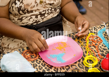 Donna che fa il tallone lacci collo. Ellis Park Street Market. Durban, Sud Africa Foto Stock