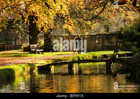 LOWER SLAUGHTER, GLOUCESTERSHIRE - 02 NOVEMBRE 2009: Camminatore di cani in passerella sul fiume Windrush in autunno, Foto Stock