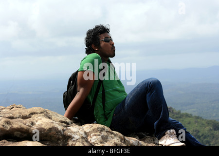 Giovane uomo seduto su di una roccia e guardando lontano Foto Stock