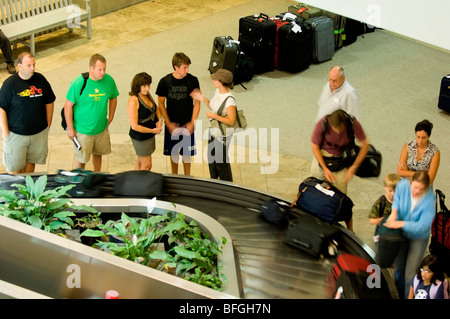 Passeggeri attendere per le loro borse presso il nastro trasportatore dei bagagli. Foto Stock