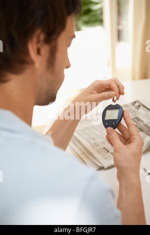 Uomo che utilizza i livelli di zucchero nel sangue Meter in salotto Foto Stock