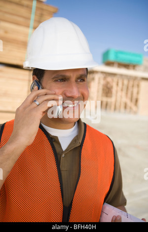 Operaio edile in piedi sul sito in costruzione e parlare in un telefono mobile Foto Stock