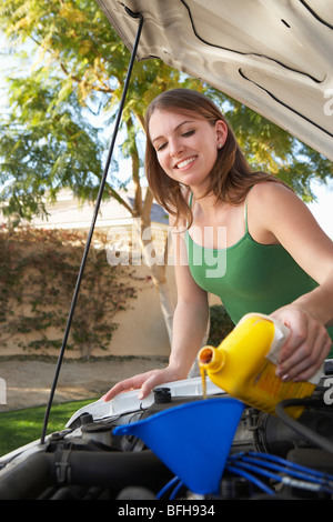 Giovane donna versando olio nel motore per auto Foto Stock