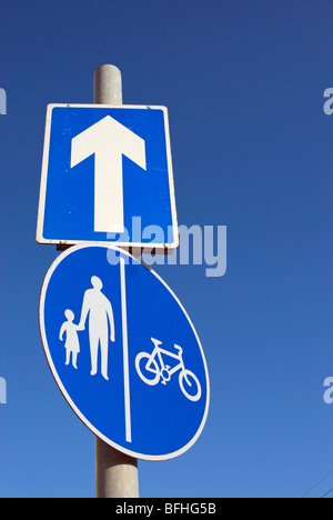 British cartelli stradali che indicano una strada a senso unico, con una freccia bianca, e corsie separate per i ciclisti e i pedoni Foto Stock