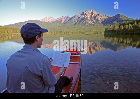 Medioevo maschio libro lettura in canoa sul lago di montagna. Foto Stock