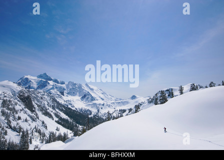 Un lone snowshoer su una soleggiata giornata di primavera a Mount Baker con Mount Shuksan in distanza Snoqualmie Foresta Nazionale di Washington (USA) Foto Stock