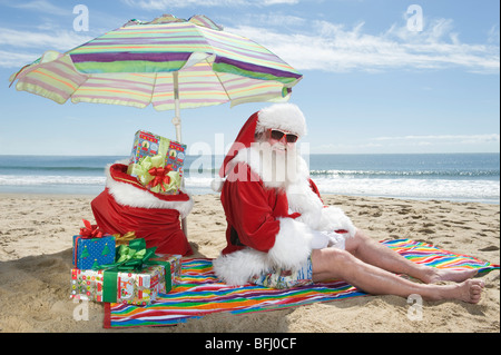 Babbo Natale si siede sotto un ombrellone in spiaggia Foto Stock