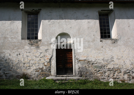 Porta di legno e due finestre di un vecchio edificio rurale. Fotografia scattata da fuori. Muro Bianco con i contrassegni di intonaco fatiscente. Ombre sulla porta. Foto Stock