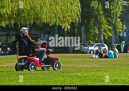 Anziano gentiluomo su uno scooter di mobilità, rilassante nel parco su una giornata d'estate Foto Stock