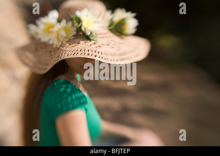 Un pelo lungo giovane donna o un adolescente che indossa un cappello di paglia ornato di fiori si siede al sole su un giorno di estate" Foto Stock