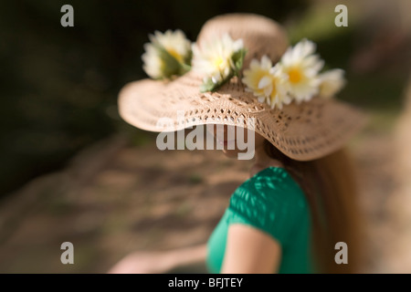 Un pelo lungo giovane donna o un adolescente che indossa un cappello di paglia ornato di fiori si siede al sole su un giorno di estate" Foto Stock