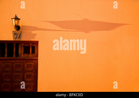 Ombra di una vecchia lampada su un muro color ocra al tramonto Foto Stock