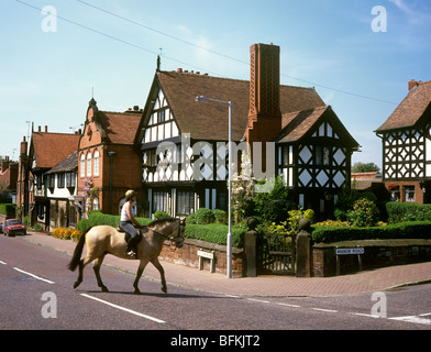 Regno Unito, Inghilterra, Wirral, Thornton Hough, Neston Road, donna di equitazione attraverso il villaggio Foto Stock