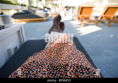 La donna posa su un patio poltrona indossando un vestito e stivali Foto Stock