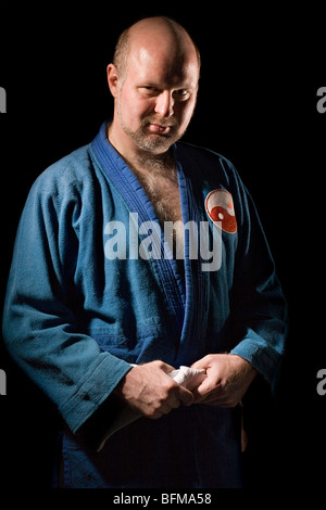 Uomo serio in blu scuro kimono tiene le mani sulla cinghia isolato su nero Foto Stock