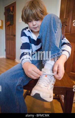 Dieci anni di vecchio ragazzo mettendo su le sue scarpe a casa, tie, legatura lacci delle scarpe di sneakers Foto Stock