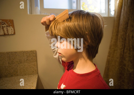 Sette anni di vecchio ragazzo pettinare i capelli nel bagno prima della scuola Foto Stock