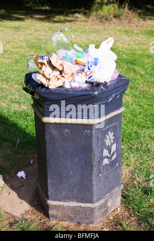 Un bidone della spazzatura in un parco pubblico traboccante di spazzatura in generale e dei contenitori di plastica. Il Dorset. In Inghilterra. Regno Unito. Foto Stock