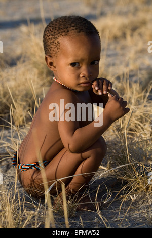 Il Botswana, Makgadikgadi. Una San bambino boscimane riproduce in erba secca, indossando solo una cintura tradizionale di perle. Foto Stock