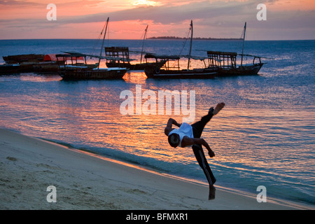 Tanzania, Zanzibar. Al tramonto, un acrobat somersaulting pratiche sulla spiaggia sabbiosa a ovest di Stone Town. Foto Stock