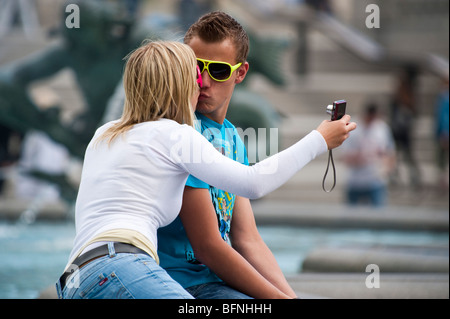 Giovane uomo e donna che indossa gli occhiali da sole divertente seduta su un confine fontana di scattare una foto di se stessi Foto Stock