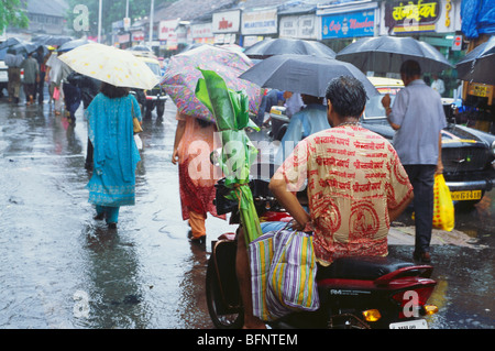 Persone con ombrelloni in monsone pioggia; sacerdote indù in moto bagnarsi; Bombay; Mumbai; Maharashtra; India; asia Foto Stock