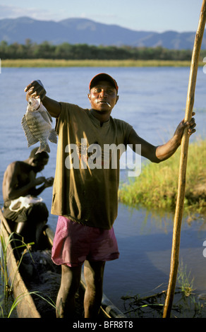 Pescatore locale in piedi nella sua piroga tenendo in mano un pesce appena pescato Foto Stock