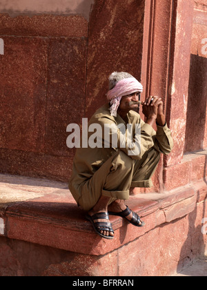 Uomo locale indossando turbante e kaki vestiti squat sul bordo di un terrazzo presso il Red Fort Agra con mani giunte Foto Stock