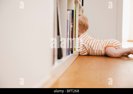 Il Bambino giacente sul piano cercando nella libreria Foto Stock