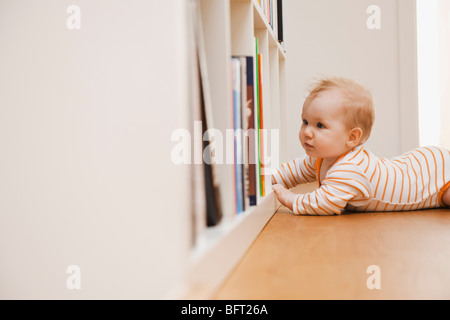 Il Bambino giacente sul piano cercando nella libreria Foto Stock