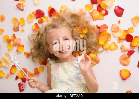 Ragazza bionda con la bacchetta magica che giace tra i petali di fiori Foto Stock