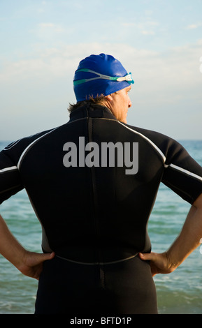 Una vista posteriore di un nuotatore muscolare o triatleta indossando una muta e cuffia per la piscina guardando al lato. Foto Stock