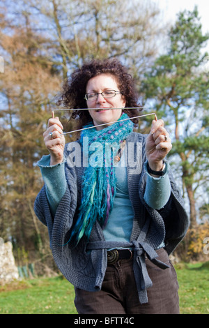 Donna sorridente serranda concentrando con L in metallo a forma di aste radioestesia esercitarsi in Rollright Stones, Warwickshire, Inghilterra Foto Stock