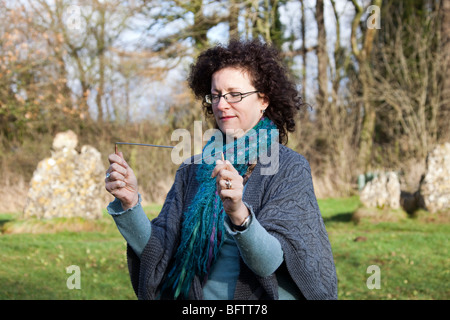 Donna con serranda L in metallo a forma di aste radioestesia esercitarsi in Rollright Stones, Warwickshire, Inghilterra. Primo piano orizzontale Foto Stock