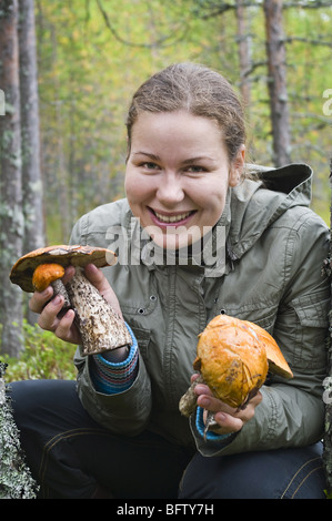 Piuttosto giovane donna che mantiene molti funghi in mani e sorriso. Lei è nella foresta. All'esterno. Foto Stock