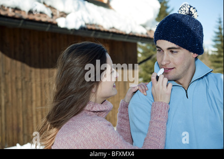 Giovane al di fuori di Ski lodge, giovane donna applicando LIP BALM di giovane Foto Stock