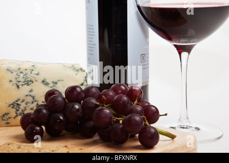 Stilton con uve rosse e crackers su una tavola di legno di formaggi accompagnato da una bottiglia e un bicchiere di vino rosso. Foto Stock