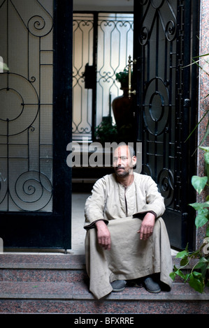 Un egiziano 'bowab' o il portiere, indossando un jellabiya, siede all'entrata frontale di un edificio residenziale nel quartiere di Maadi del Cairo, Egitto. Foto Stock