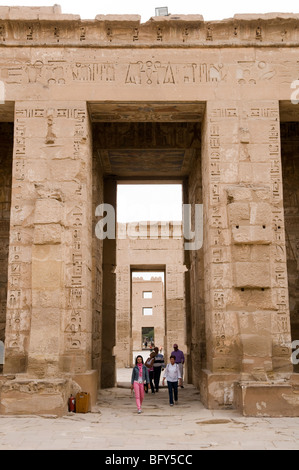I turisti passano attraverso una porta o un pilone nella navata centrale all'interno del tempio di Habu Medenet nei pressi di Luxor in Egitto. Foto Stock