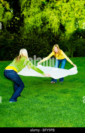 Le donne che stabilisce una coperta verso il basso sull'erba Foto Stock